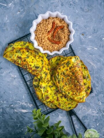 a couple of Methi Ghavan | Fenugreek Rice Flour Crepes placed over a wire rack with a side of peanut chutney