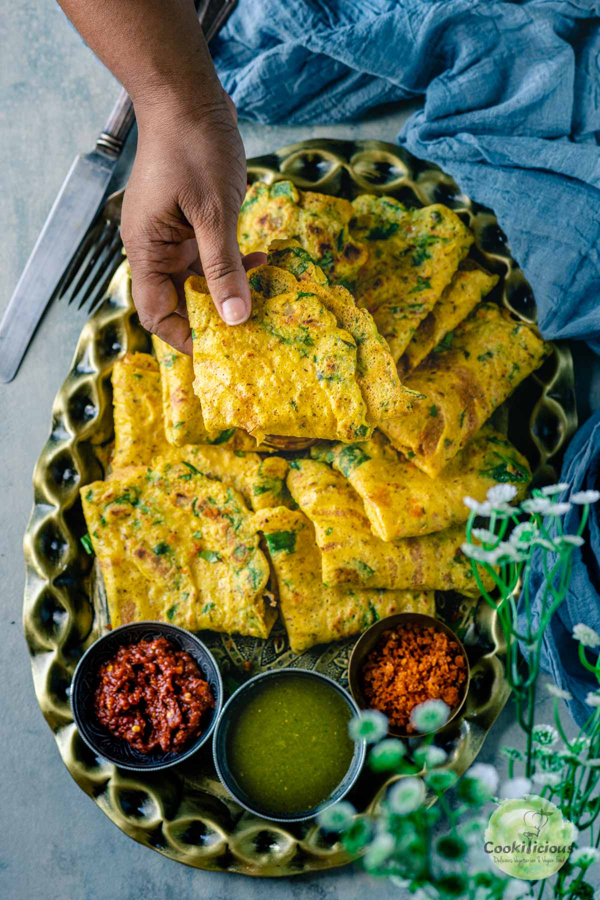 a hand picking up one Moong Dal Chilla from a tray.