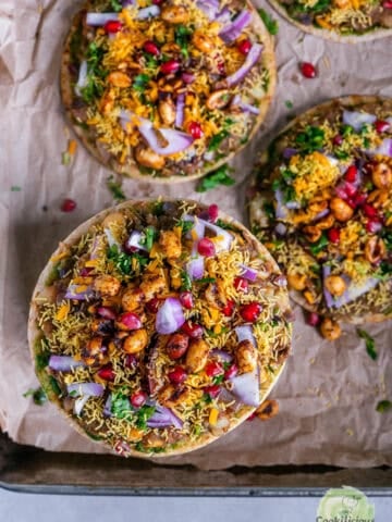 Cheesy Dabeli Pizza on mini pita bread with dabeli masala, pomegranate seeds, spiced peanuts, and crispy sev - easy Indian street food fusion snack.